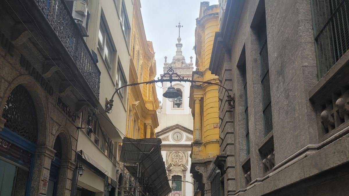Narrow historic alley in downtown Rio de Janeiro framed by colonial buildings, leading to a baroque church