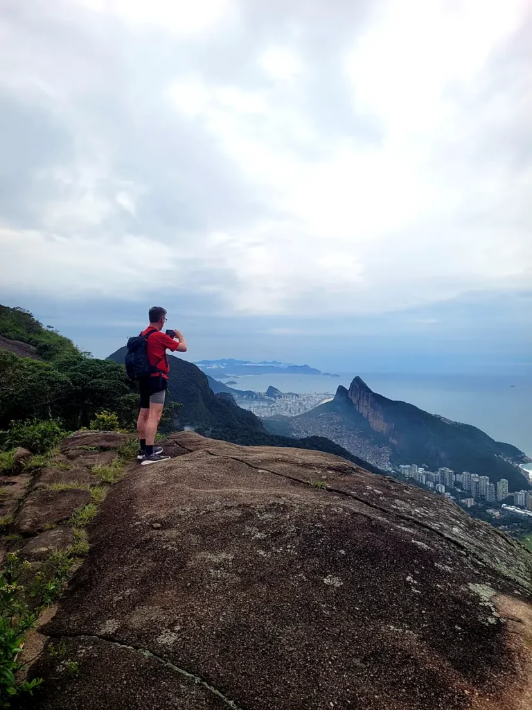 Hiker photographing the view of Leblon and Dois Irmãos from a trail in Rio’s Tijuca National Park
